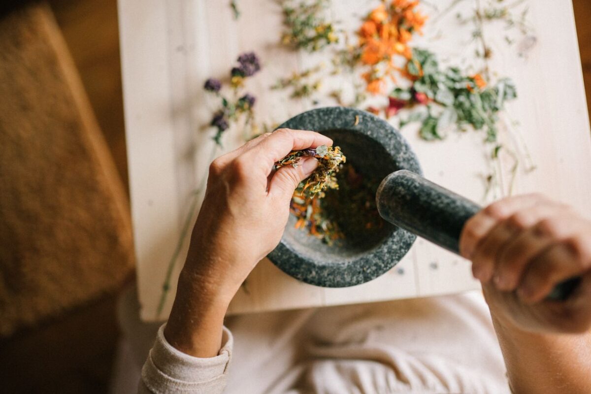 expertise-01 Top view of hands grinding dried herbs using a mortar and pestle on a wooden table.